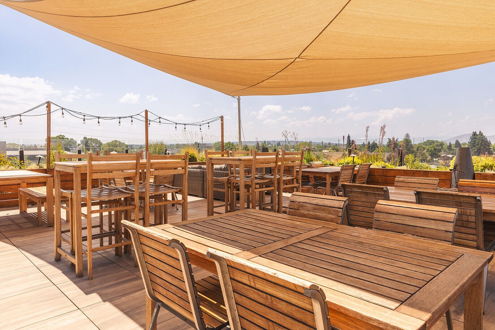 An outdoor patio area with wooden tables and chairs, string lights, and a view of the landscape.