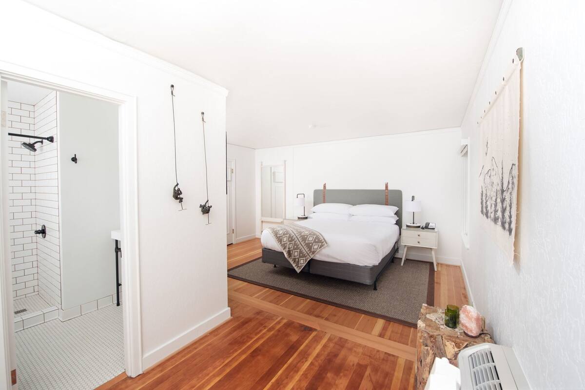 A hotel room with a bed, bedside tables, a shower, and a small rug.