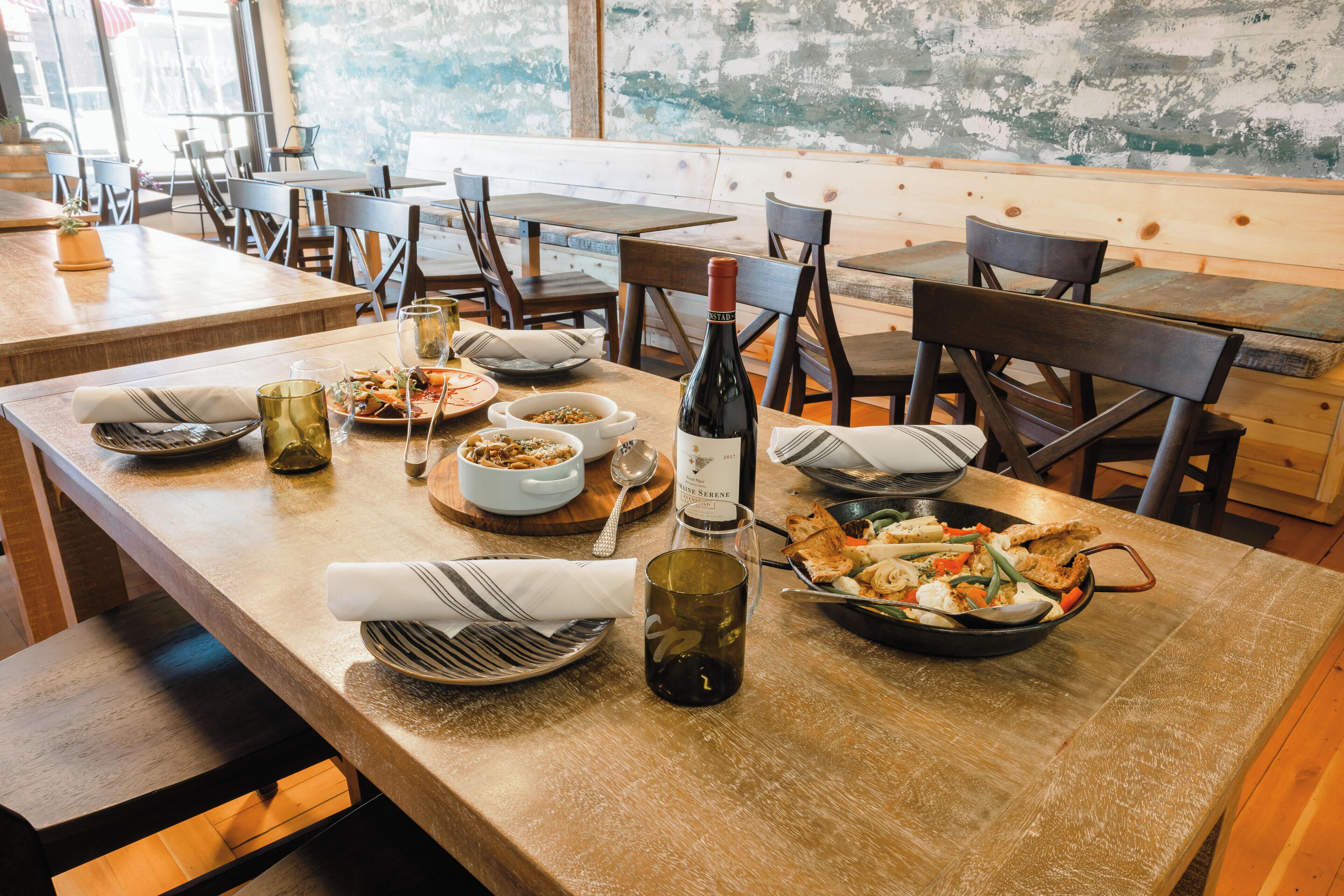 Une salle à manger de restaurant avec des tables et des chaises en bois, ainsi qu’une variété de plats et de boissons disposés sur les tables.