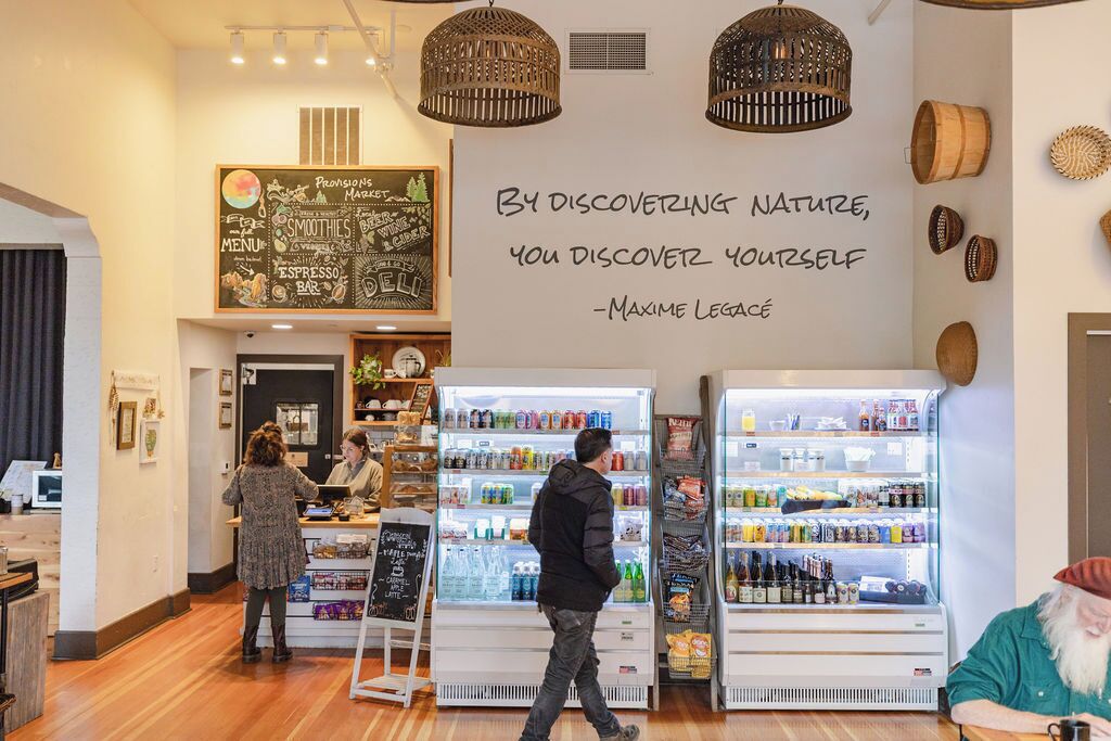 A café interior with a menu board, beverage dispensers, and a quote on the wall.