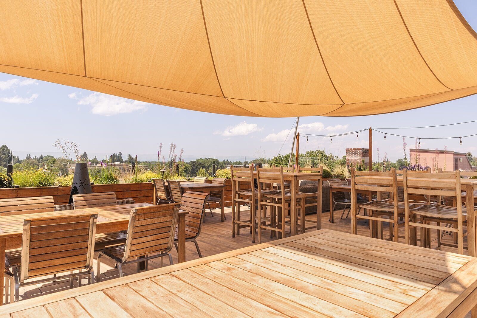 Un patio al aire libre con mesas y sillas de madera, una parrilla y un toldo grande que proporciona sombra.