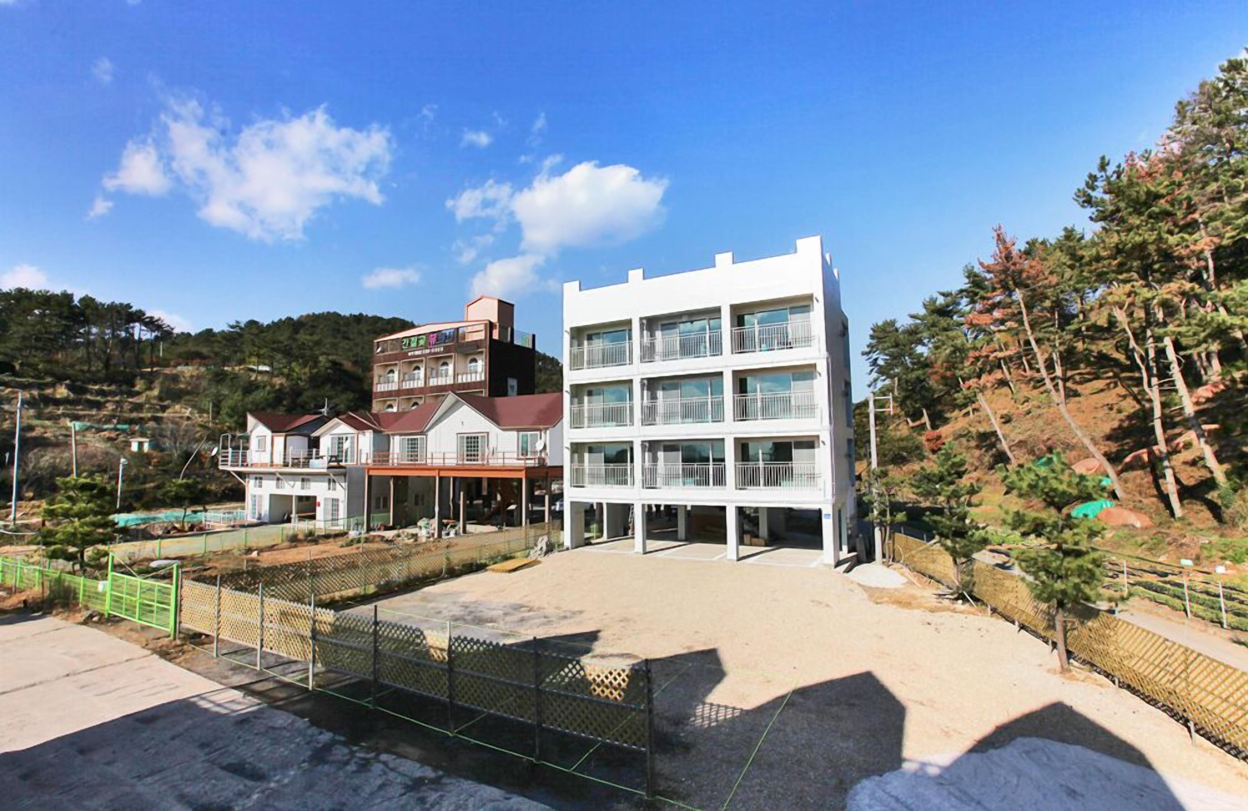 A modern building with multiple floors, a flat roof, and a large open area in front.
