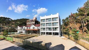 A modern building with multiple floors, a flat roof, and a large open area in front.