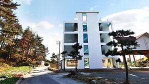 A modern multi-story building with large windows and a flat roof, surrounded by trees and a clear sky. - Ulsan Ganjeolgot View Pension (Ulsan)