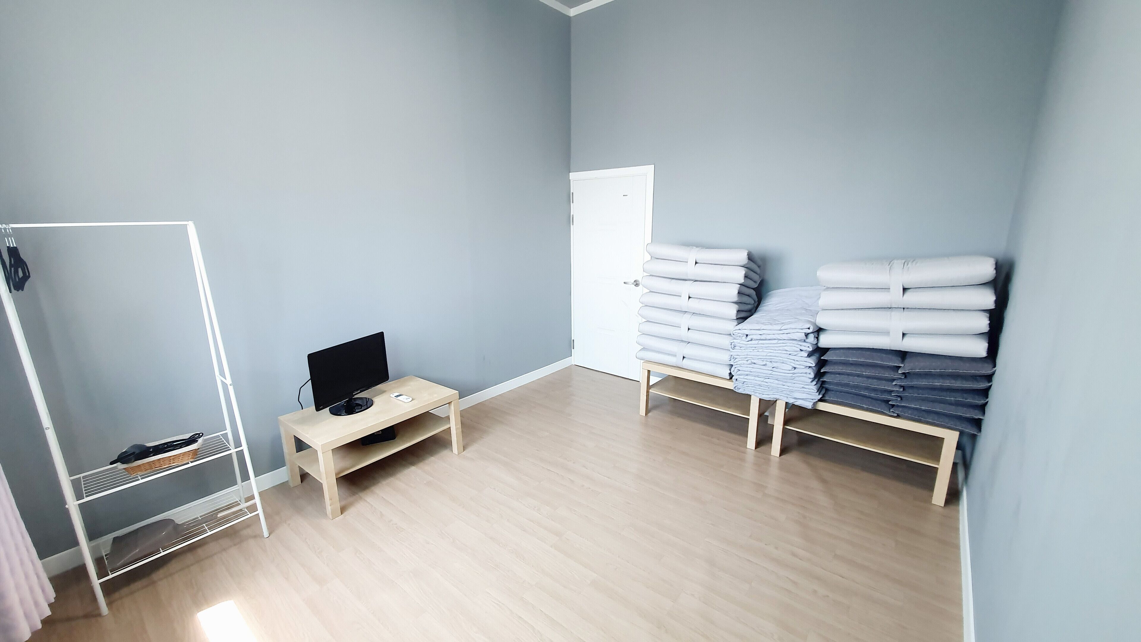 A room with a wooden floor, a desk with a computer, a white wardrobe, and a shelf with folded towels.