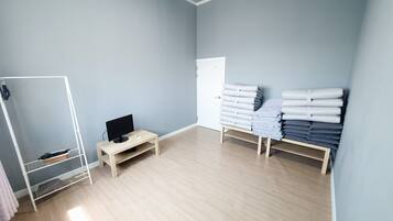 A room with a wooden floor, a desk with a computer, a white wardrobe, and a shelf with folded towels.