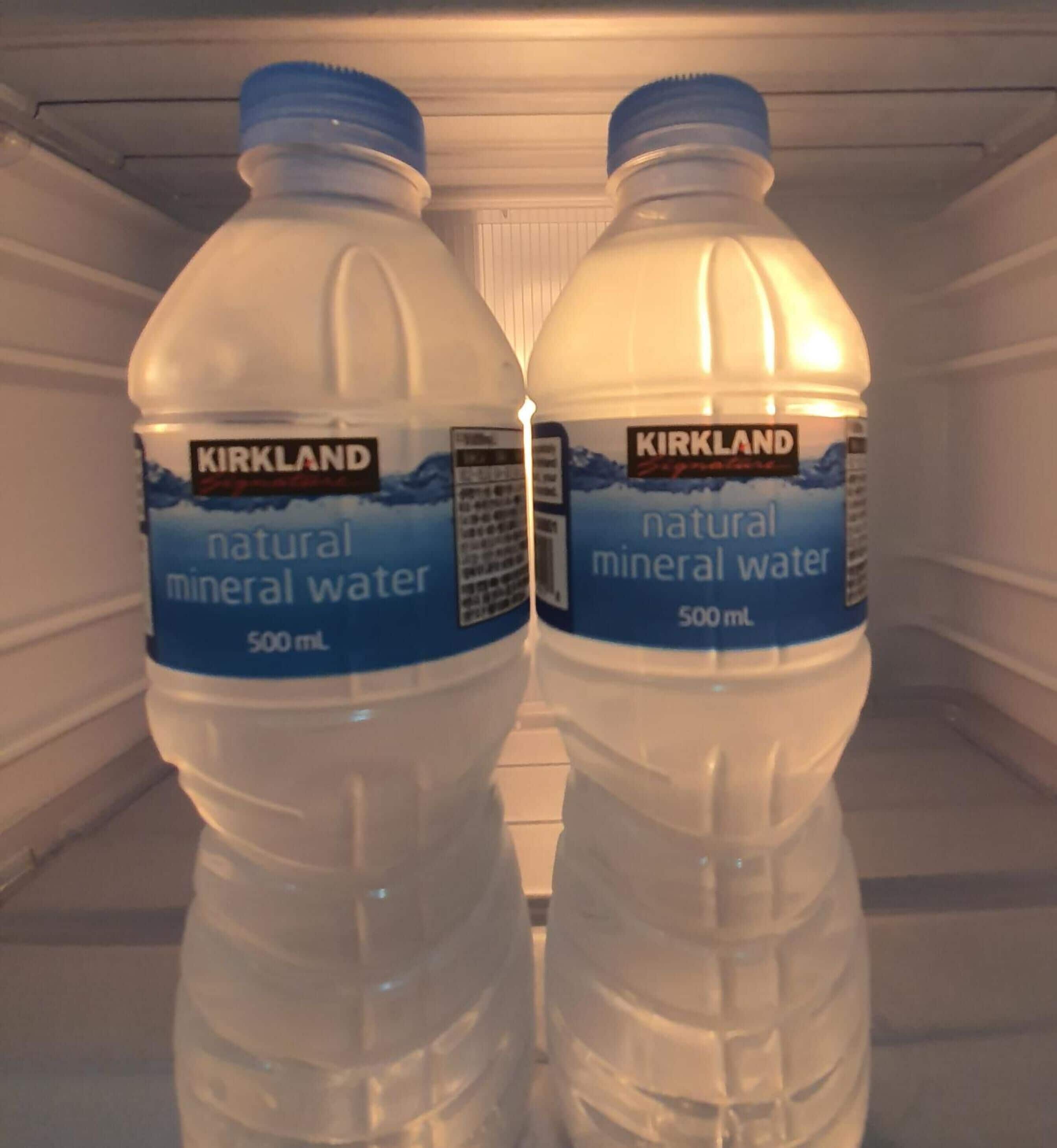 Dos botellas de 500 ml de agua mineral natural Kirkland Signature en un refrigerador.