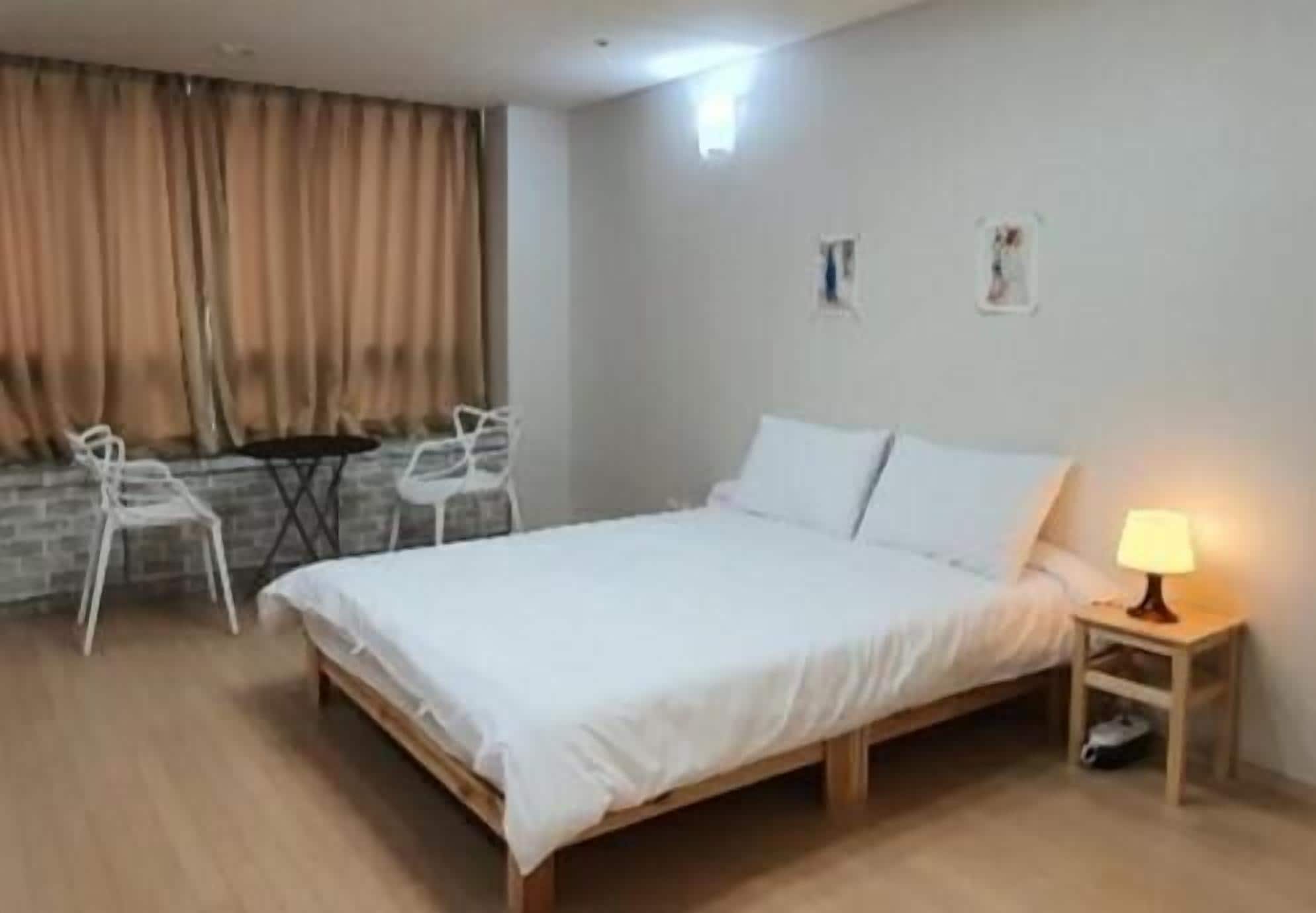 Une chambre à coucher avec un lit en bois, une literie blanche, une petite table de chevet avec une lampe et une fenêtre avec des rideaux.