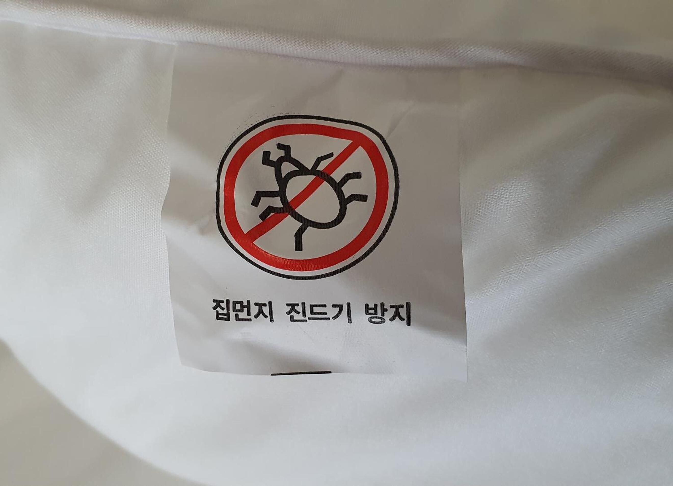 A white fabric with a label featuring a prohibition sign and Korean text.