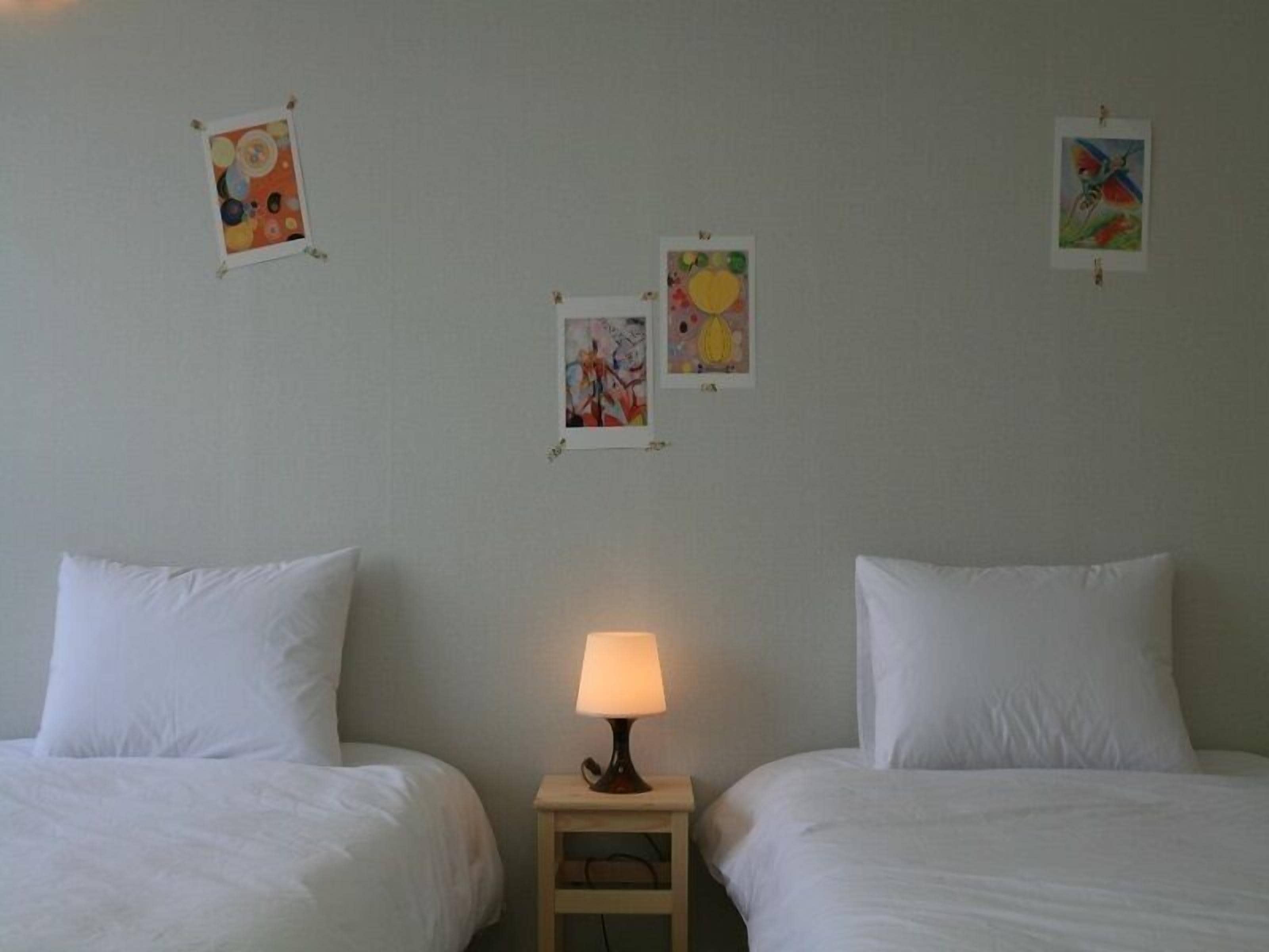 Et hotelværelse med to senge, et natbord med en lampe og tre billeder hængt på væggen.
