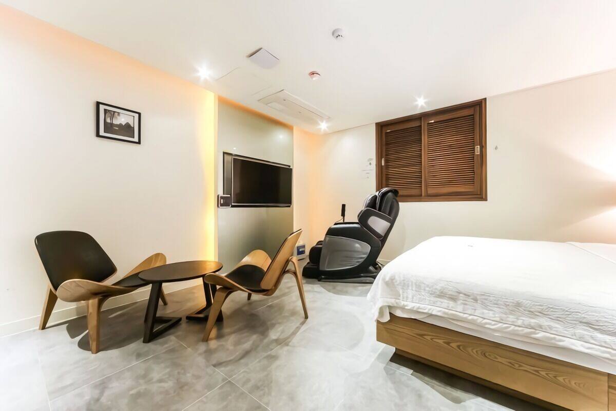 A hotel room with a bed, a TV mounted on the wall, a massage chair, and a small table with chairs.