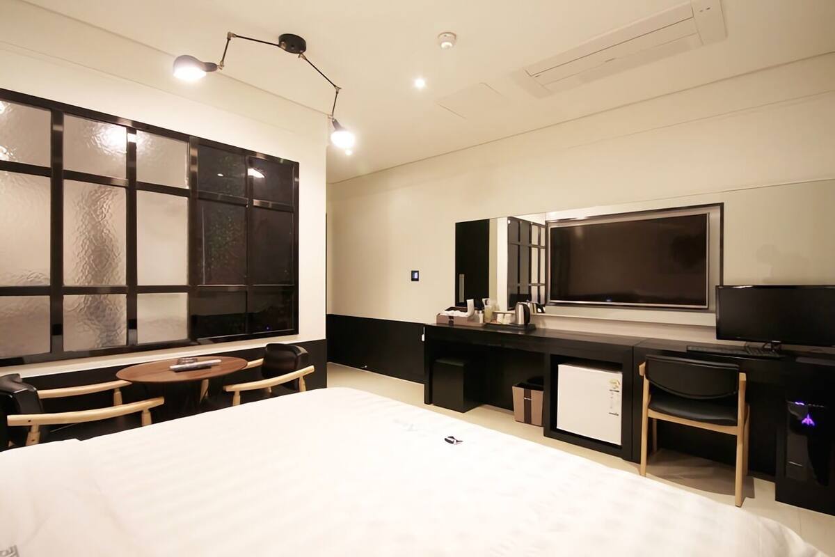 A modern hotel room with a large bed, a desk with a computer, a TV, and a seating area with a table and chairs.