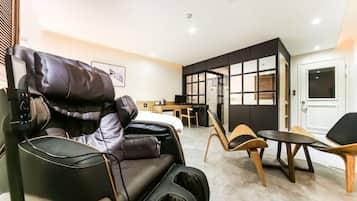 Una silla de masaje, una mesita y un sofá en una habitación moderna con suelo de baldosas y puerta corredera.