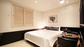 A hotel room with a large bed, a bedside table, a chair, a desk, and a wall-mounted TV.