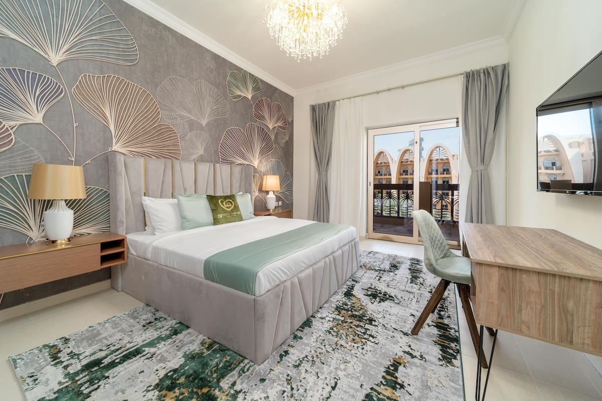 A modern hotel room with a large bed, a desk, and a balcony with a view of the building.