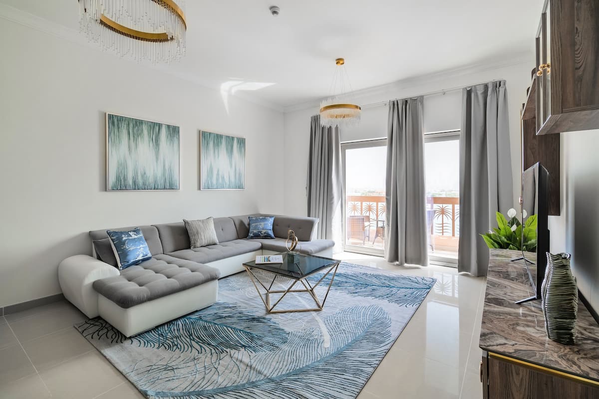 A modern living room with a sectional sofa, a glass coffee table, and a large window with curtains.