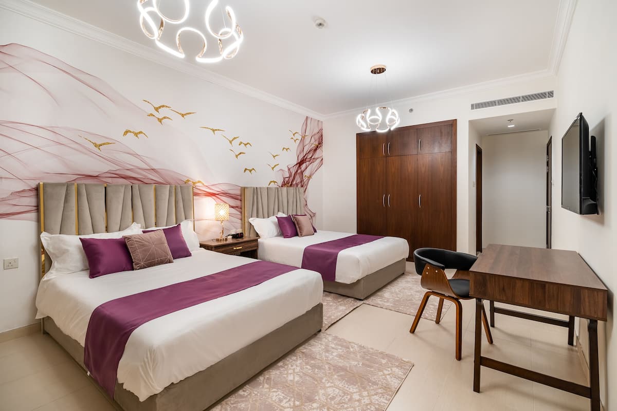 A modern hotel room with two beds, a desk, and a TV.