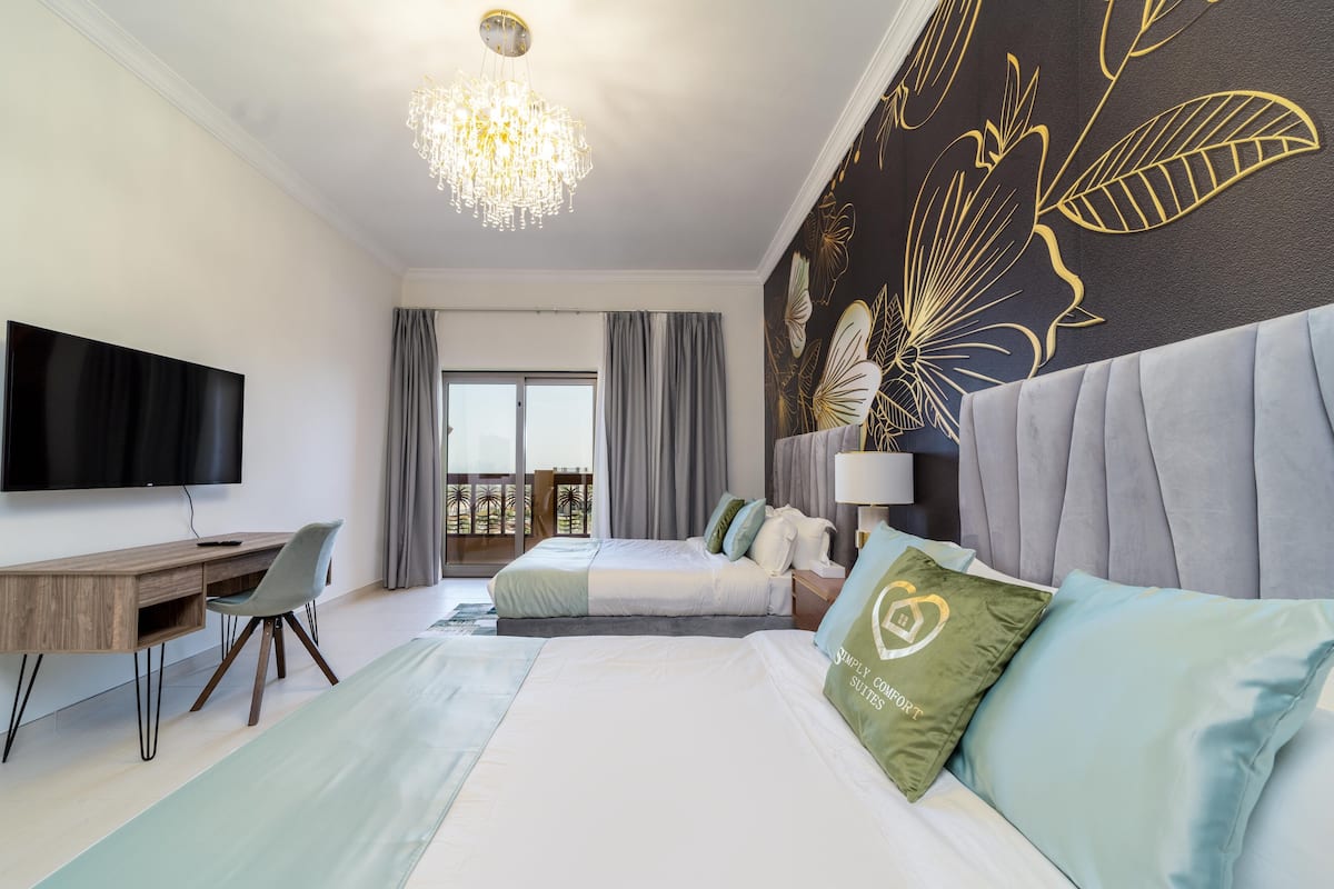 A hotel room with a large bed, a desk, a television, and a balcony with curtains.