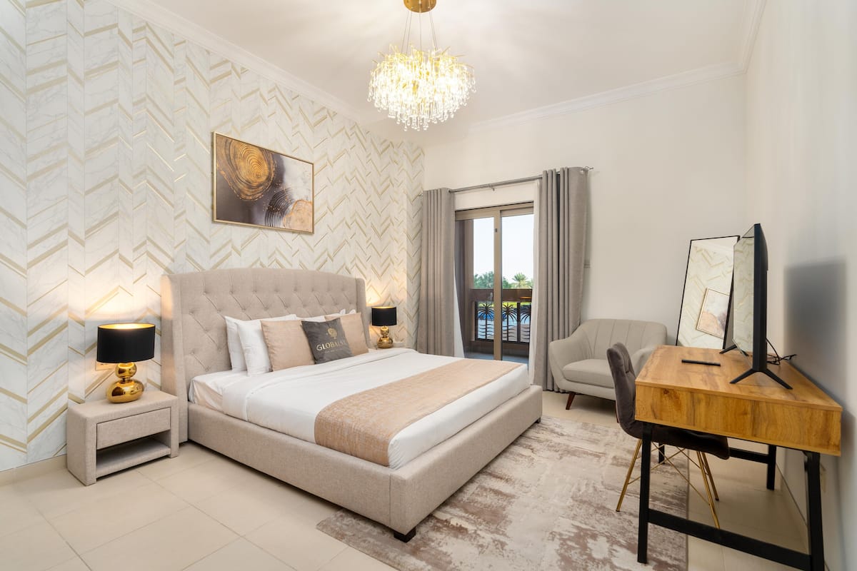 A modern bedroom with a large bed, bedside lamps, a wooden desk, and a view of the outdoors.