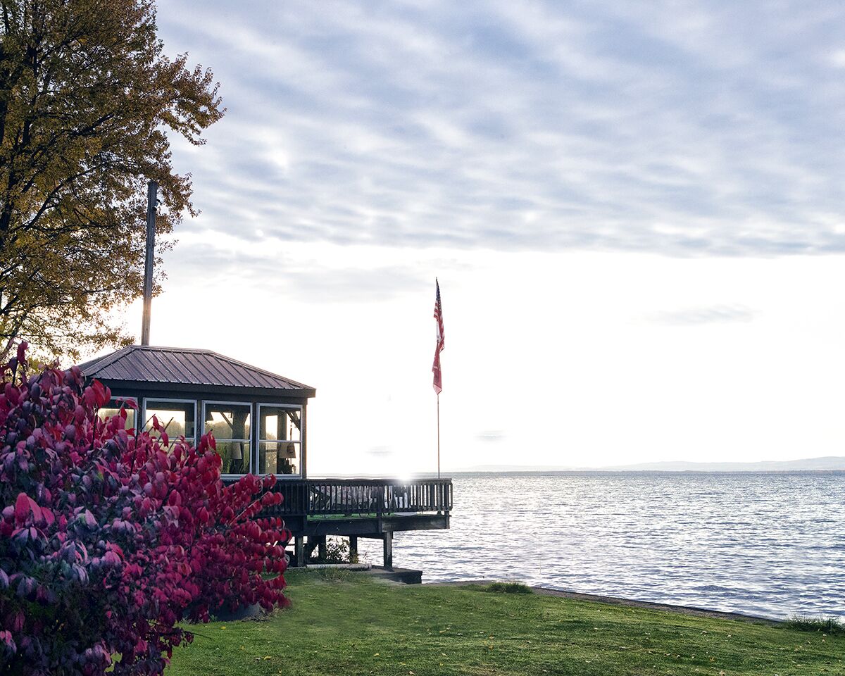 A gazebo with a view of the water, a flag, and lush greenery.