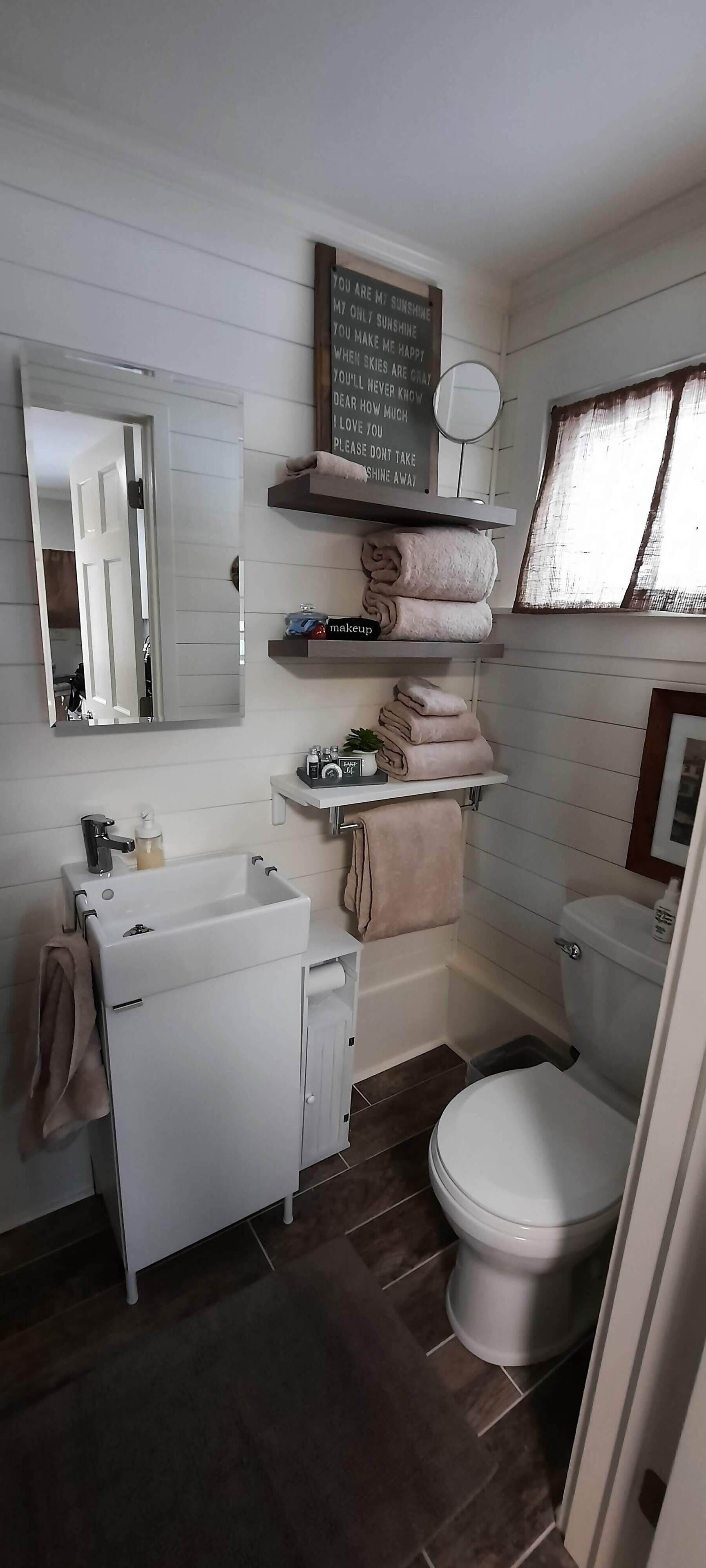 A bathroom with a white sink, mirror, and toilet. There are shelves with towels and toiletries.