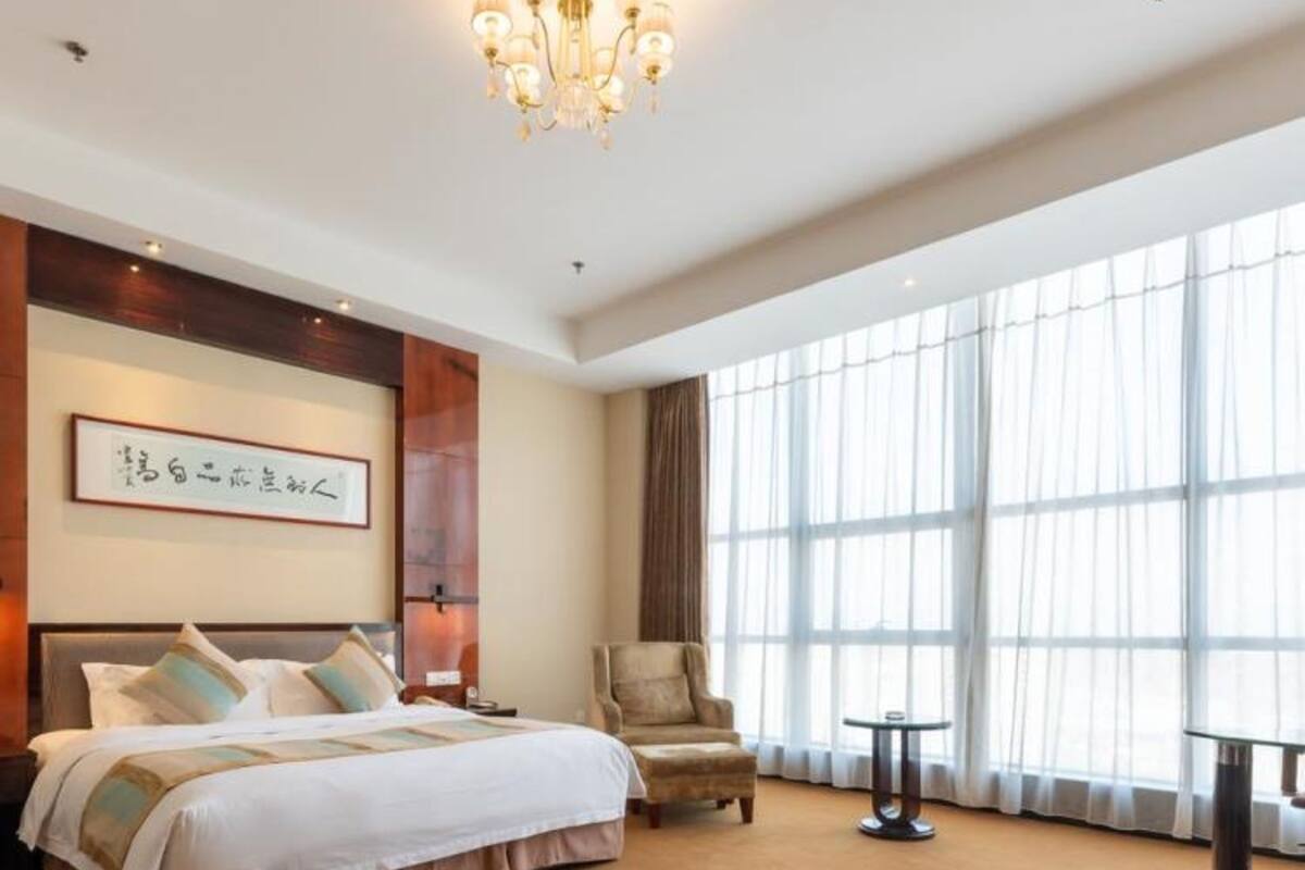 Ein Hotelzimmer mit einem großen Bett, einem Sessel, einem kleinen Tisch und einem großen Fenster mit Vorhängen.