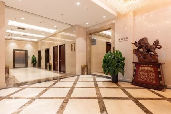 A hotel lobby with a tiled floor, a reception desk, a statue, and a sign indicating a restaurant.