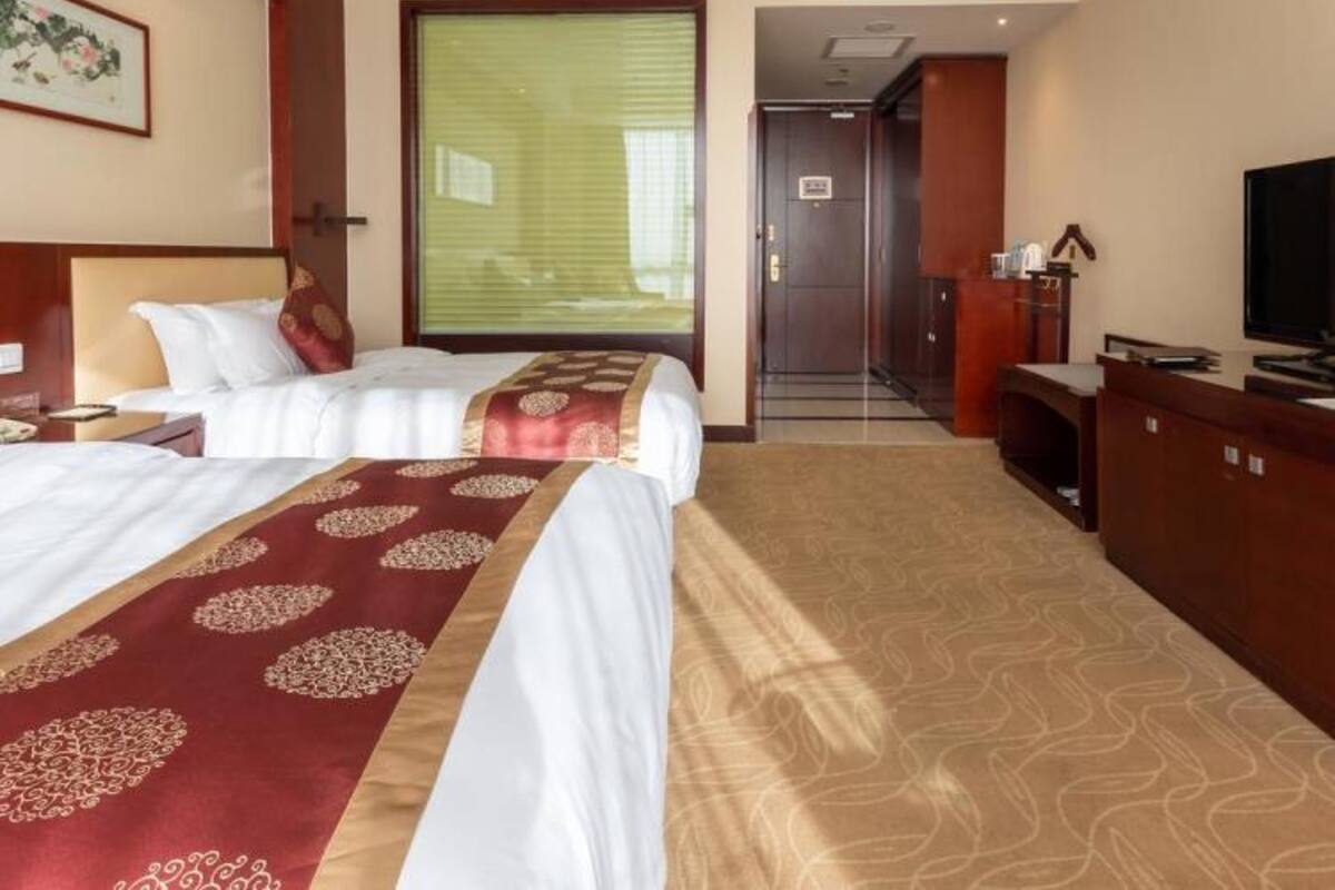 Ein Hotelzimmer mit einem großen Bett, einem Schreibtisch, einem Fernseher und einer Tür zu einem Flur.