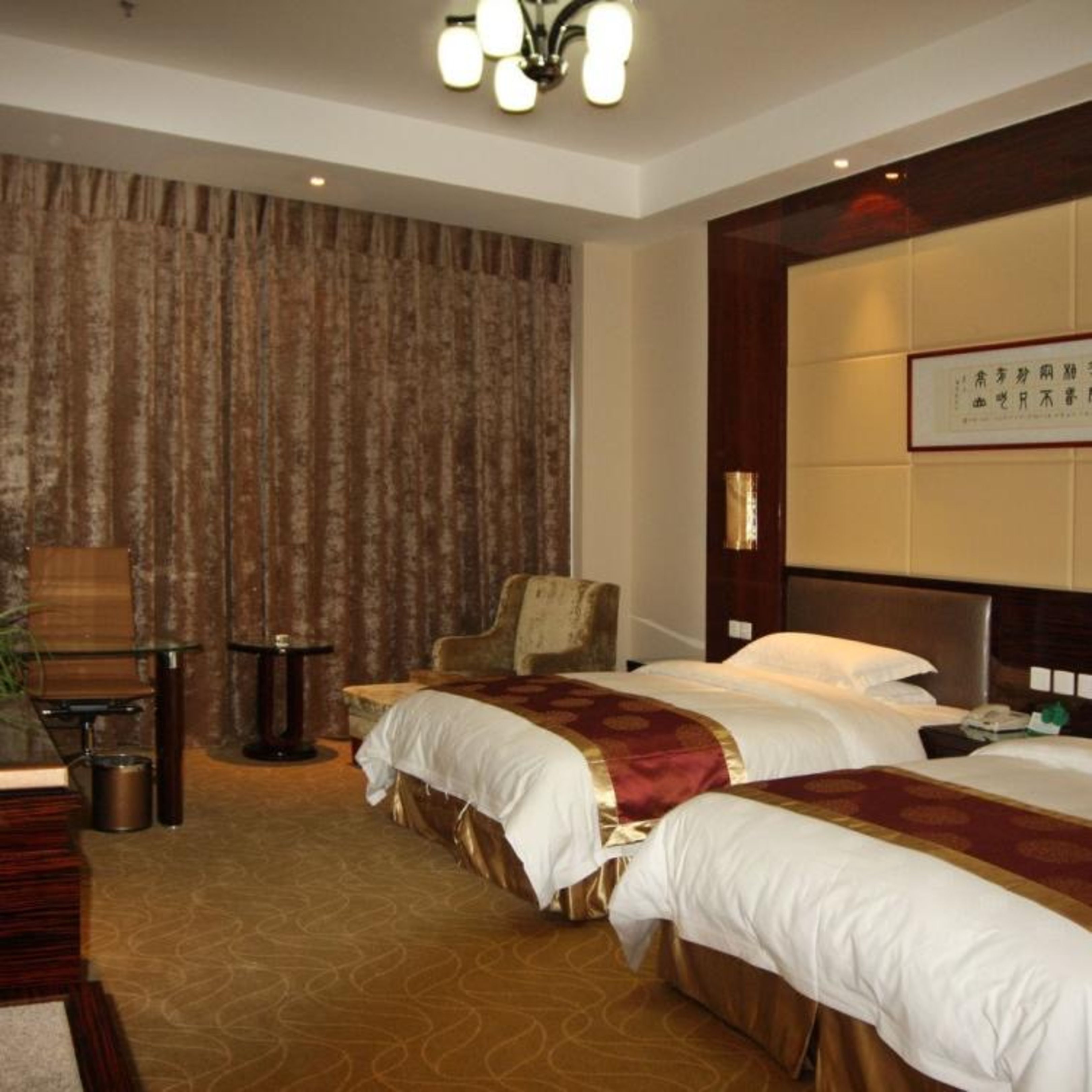 A hotel room with two beds, a chair, a desk, and a large wall-mounted TV.