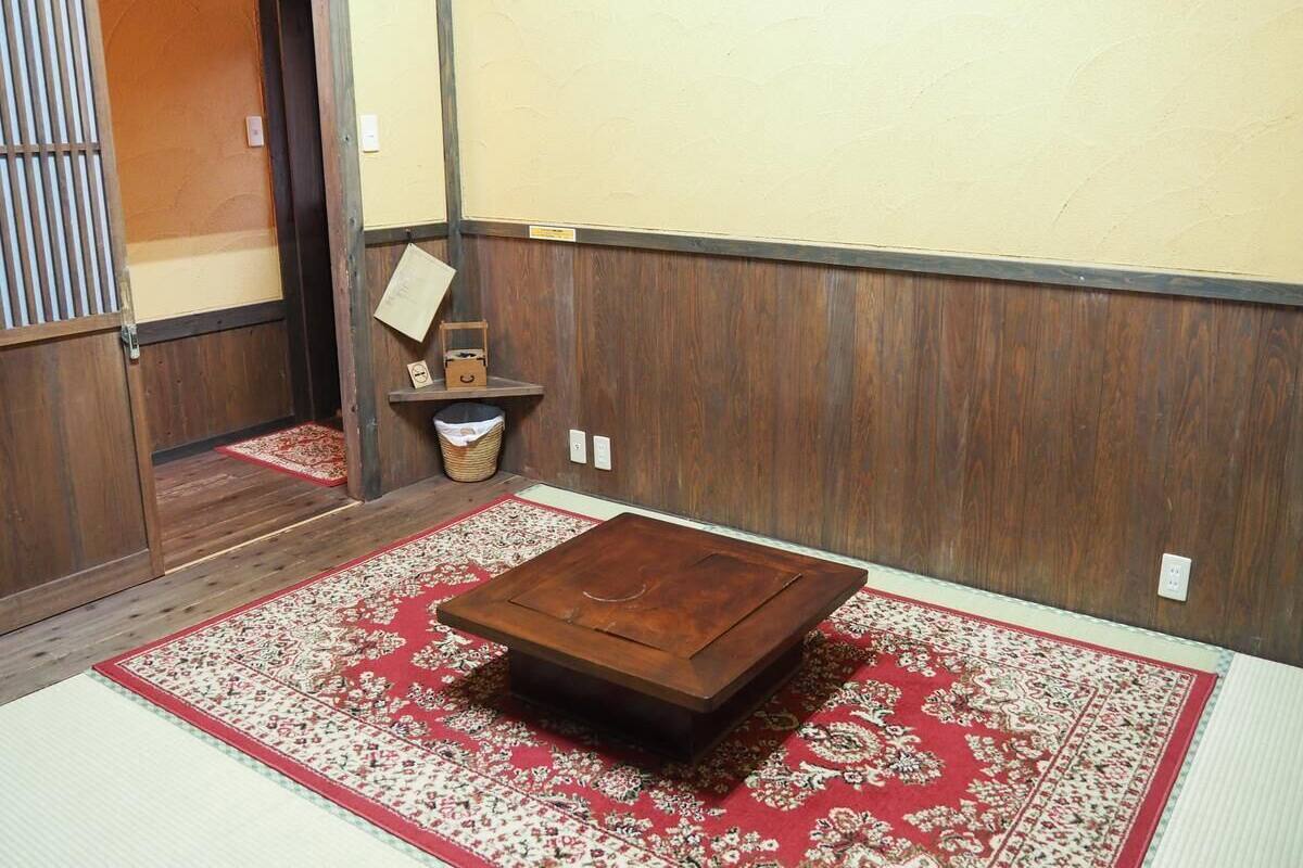 Een traditionele Japanse kamer met tatami vloerbedekking, een houten salontafel en een rood tapijt met een patroon.