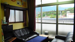 Una sala de estar con un sofá de cuero negro, una mesa de centro de madera y un televisor. Se ve una ventana con vistas a un puente y vegetación.