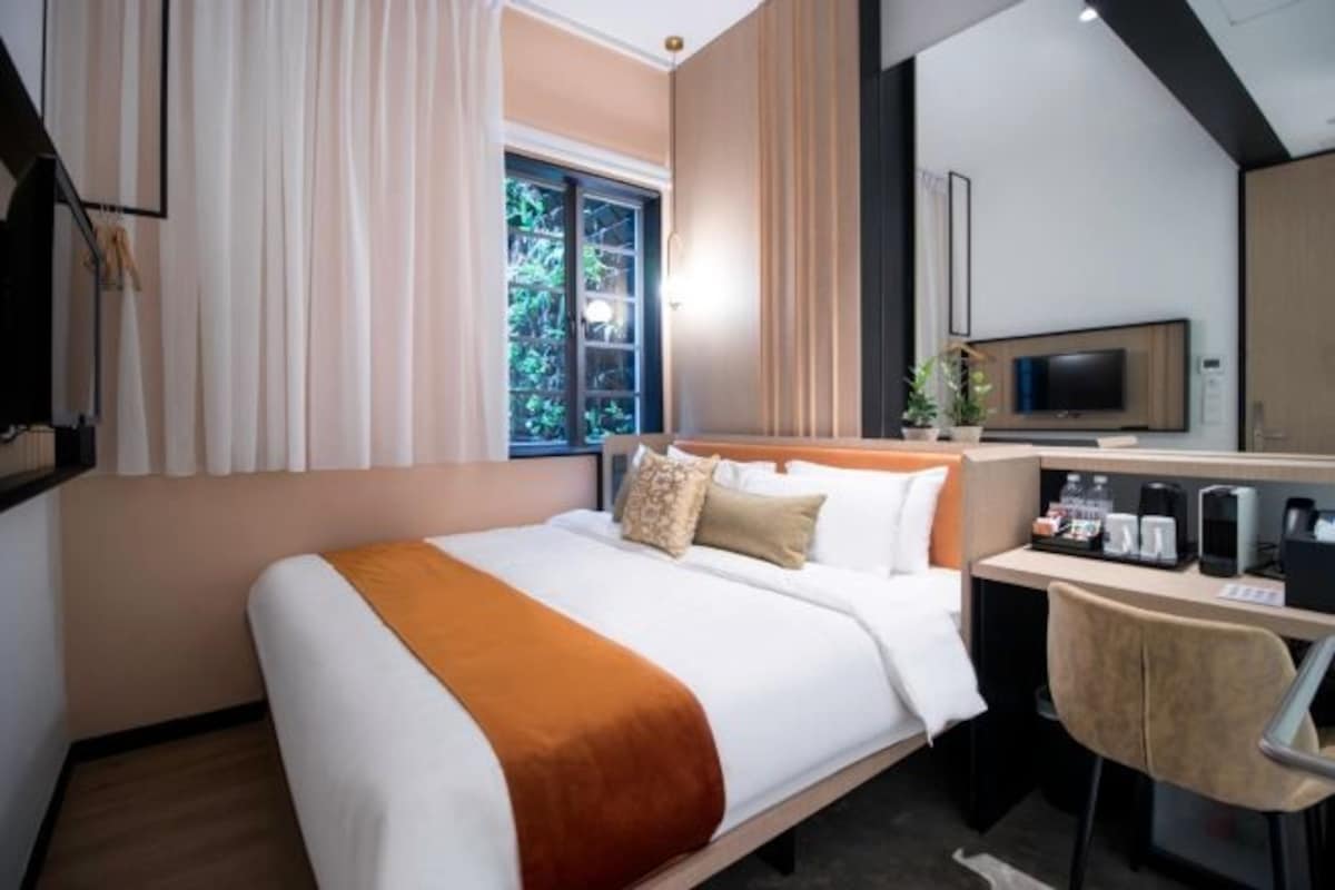 A hotel room with a bed, a desk, a television, and a window with curtains.