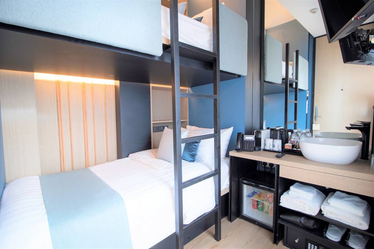 Une chambre d’hôtel moderne équipée d’un lit superposé, d’un bureau avec un lavabo et d’un mini-bar.