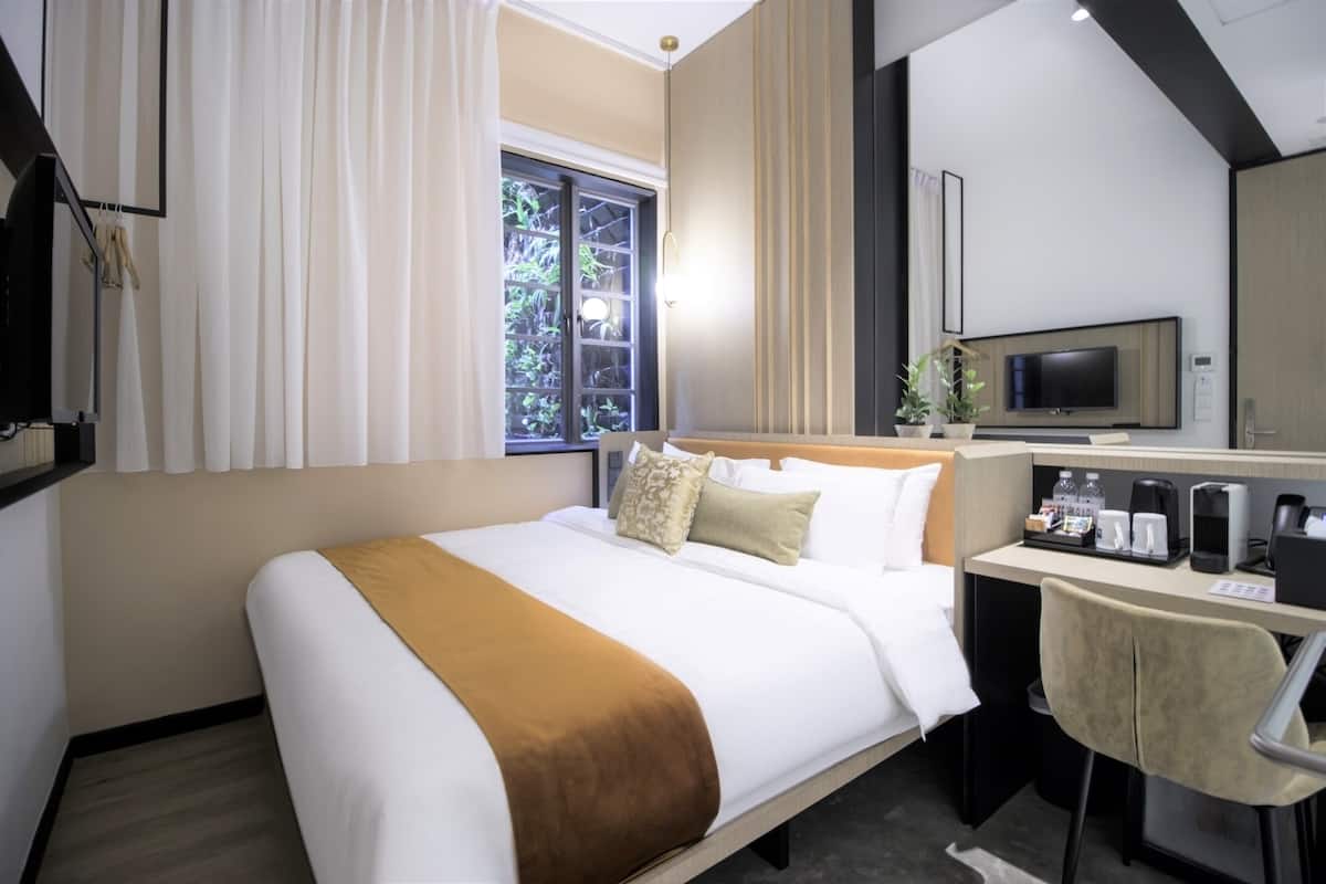 Une chambre d’hôtel avec un lit, un bureau avec un ordinateur, une télévision et une fenêtre avec des rideaux.