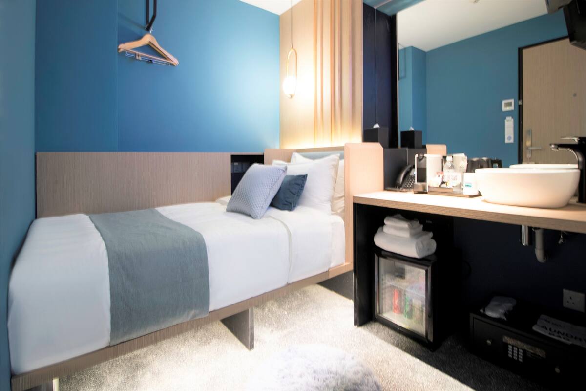 Une chambre d’hôtel moderne équipée d’un lit, d’un grand miroir, d’un lavabo et d’une armoire.