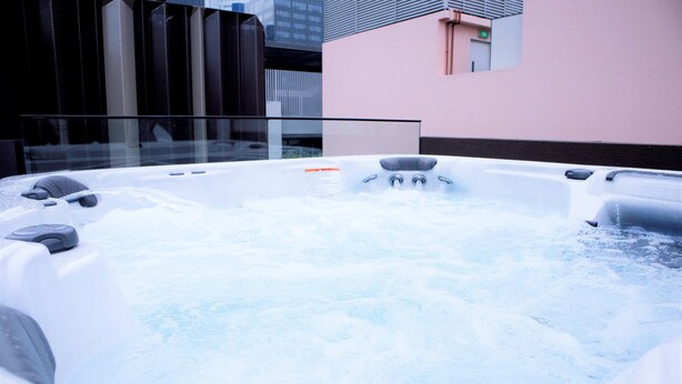 Un bain à remous avec jets, entouré d’une rambarde en verre, avec une vue sur le paysage urbain en arrière-plan.