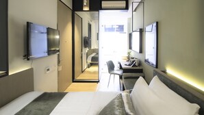 Une chambre d’hôtel moderne équipée d’un lit, d’un bureau, d’une chaise et d’un téléviseur fixé au mur.