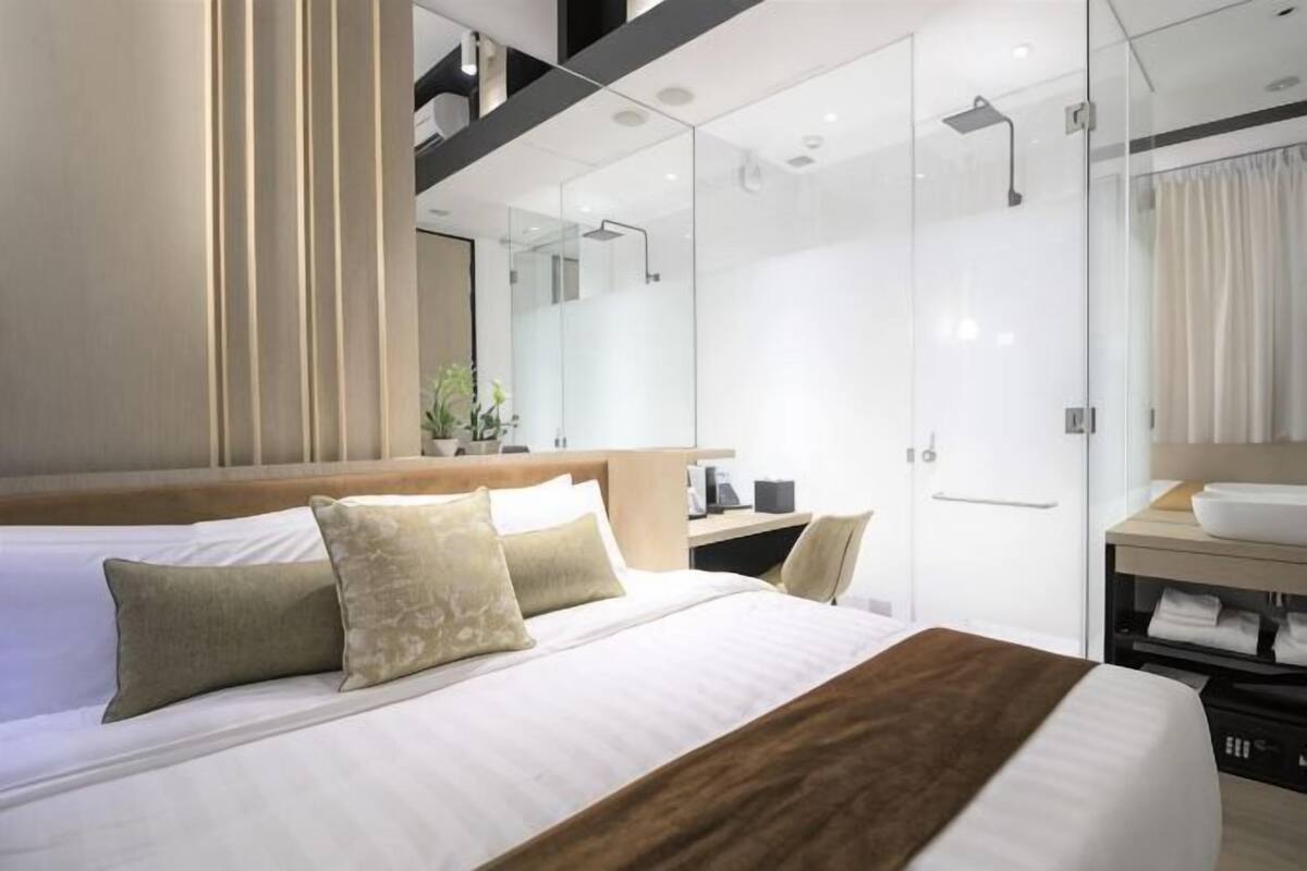 Une chambre d’hôtel moderne avec un grand lit, un miroir, une douche et un meuble-lavabo dans la salle de bain.