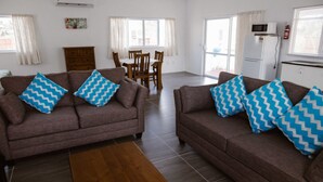 A living room with two sofas, each with blue zigzag cushions, a wooden coffee table, and a dining area with a table and chairs. - Charlie's Villas (Rarotonga)