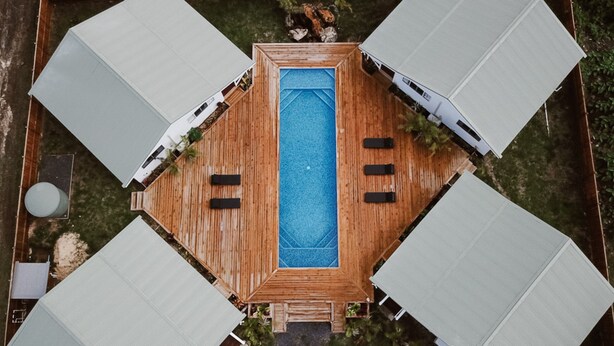 A top-down view of a rectangular pool surrounded by four white tents with black furniture. - Charlie's Villas (Rarotonga)