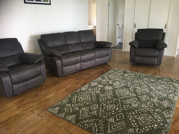 A living room with a dark brown leather sofa, two leather armchairs, and a patterned green rug on a wooden floor.