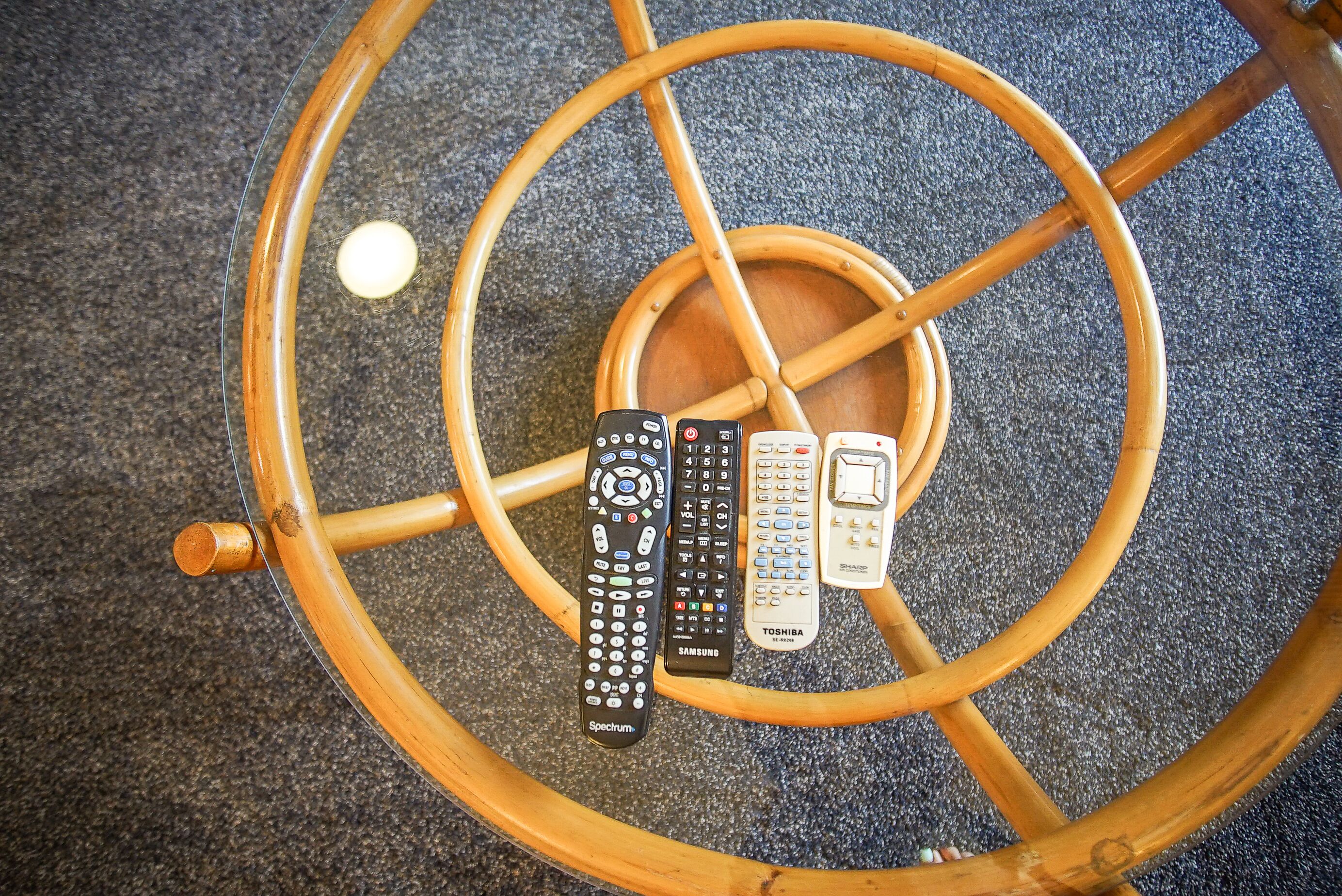 A round wooden table with four remote controls placed on it.