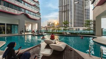 A swimming pool area with lounge chairs, a poolside seating area, and a view of high-rise buildings in the background.