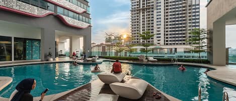 A swimming pool area with lounge chairs, a poolside seating area, and a view of high-rise buildings in the background.