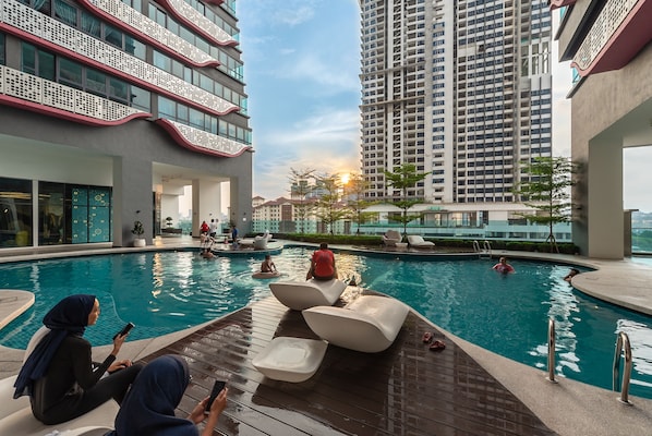 A swimming pool area with lounge chairs, a poolside seating area, and a view of high-rise buildings in the background.