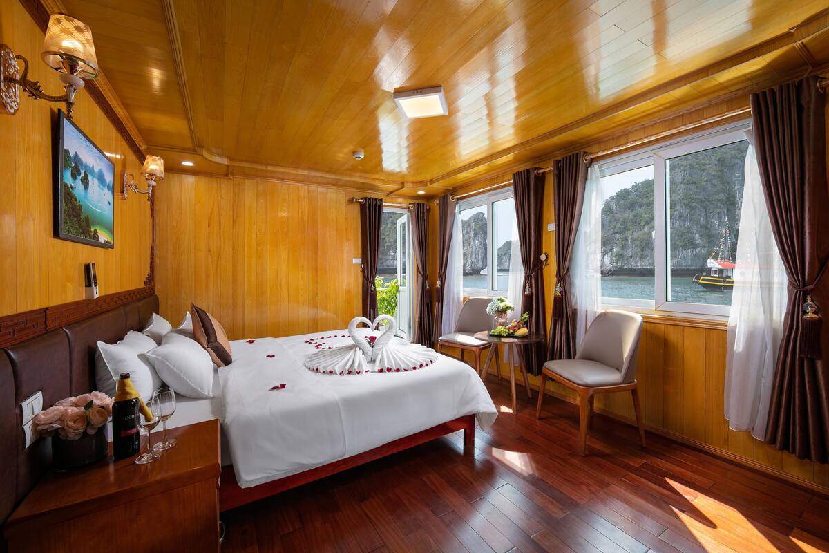 A hotel room with a wooden interior, a bed with white linens, a small table with a chair, and a large window with curtains.