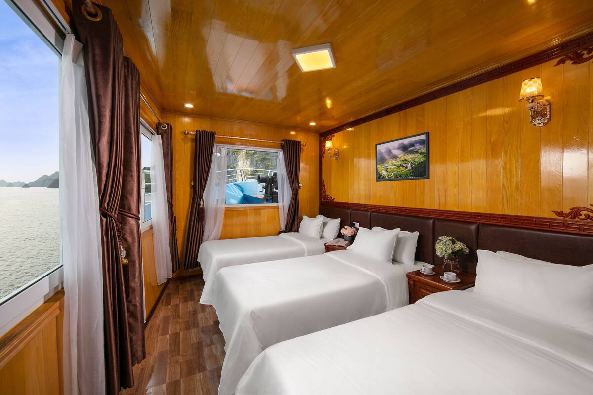 A cabin with three beds, wooden paneling, a painting, and a view of the sea.