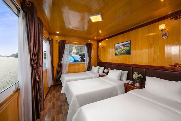 A cabin with three beds, wooden paneling, a painting, and a view of the sea.