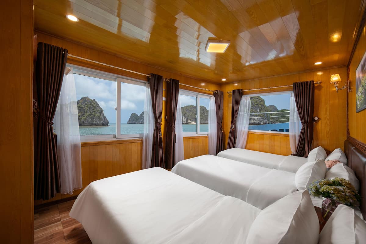 A cabin with two beds, wooden walls, large windows, and a view of the sea.