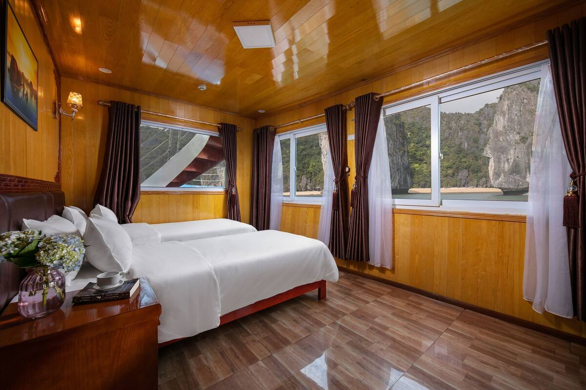 A room with a bed, a nightstand, a vase with flowers, and a window with curtains.